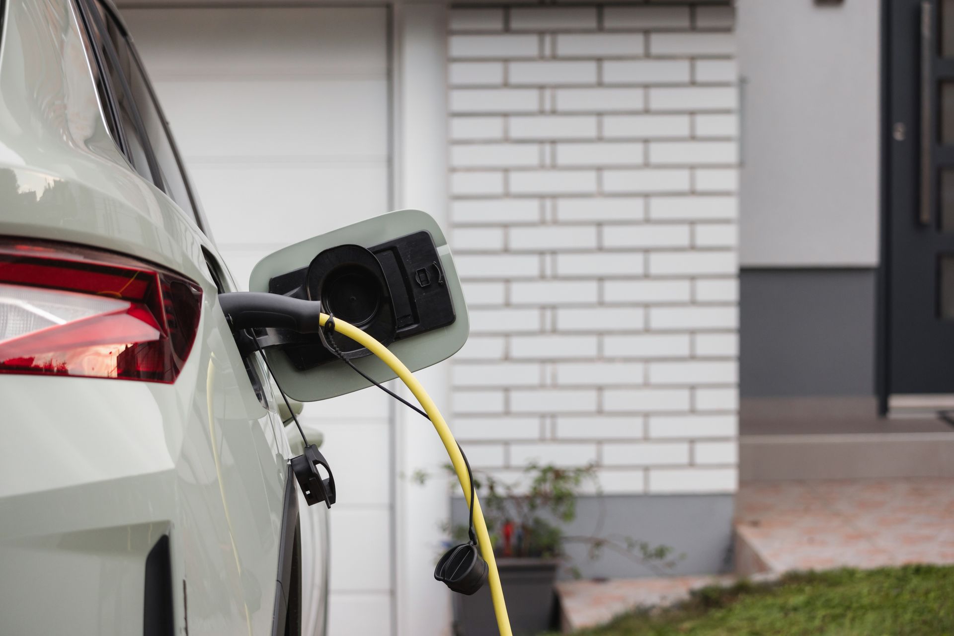 Electric car charging with yellow cable plugged into a white vehicle outdoors
