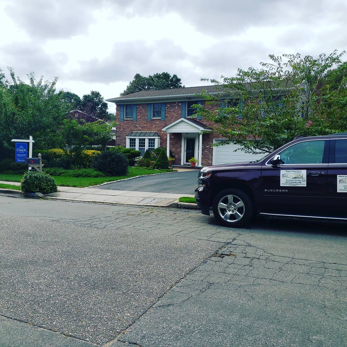 Brick two-story house with a porch and driveway, partly blocked by a dark SUV in the foreground.