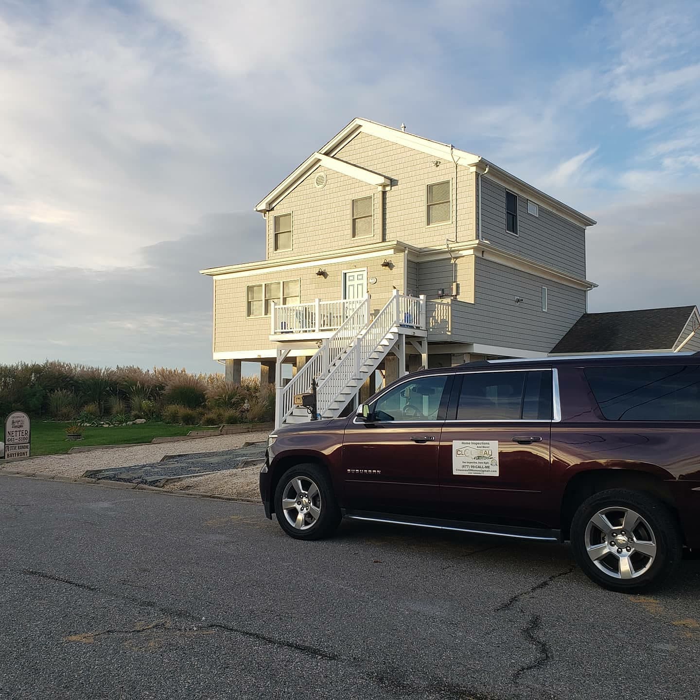 Two-story beige house near the coast with a maroon SUV parked in front at sunset
