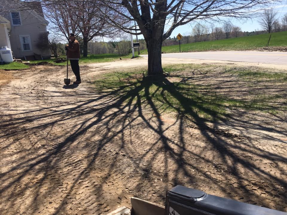 A person is standing in front of a tree with a shovel in their hand.