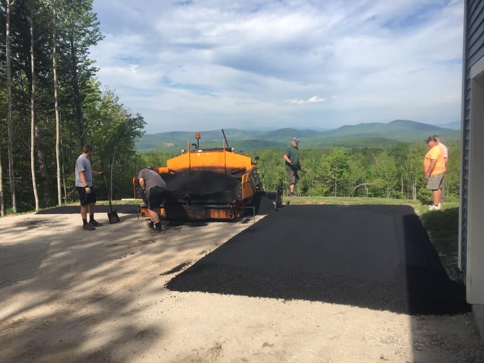 A group of people are working on a driveway with mountains in the background.
