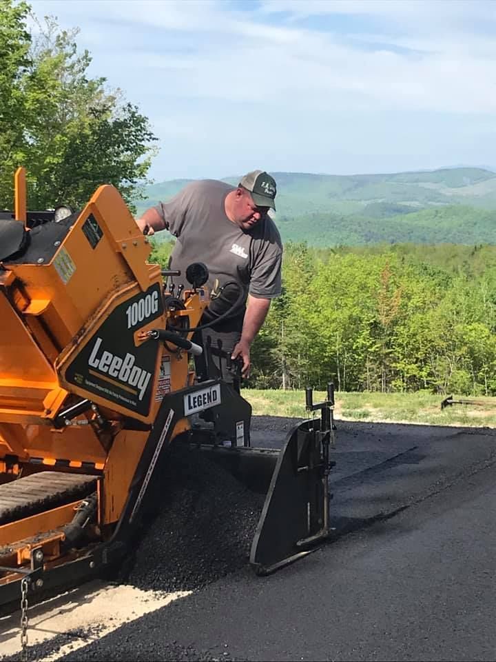A man is using a machine to spread asphalt on a road.