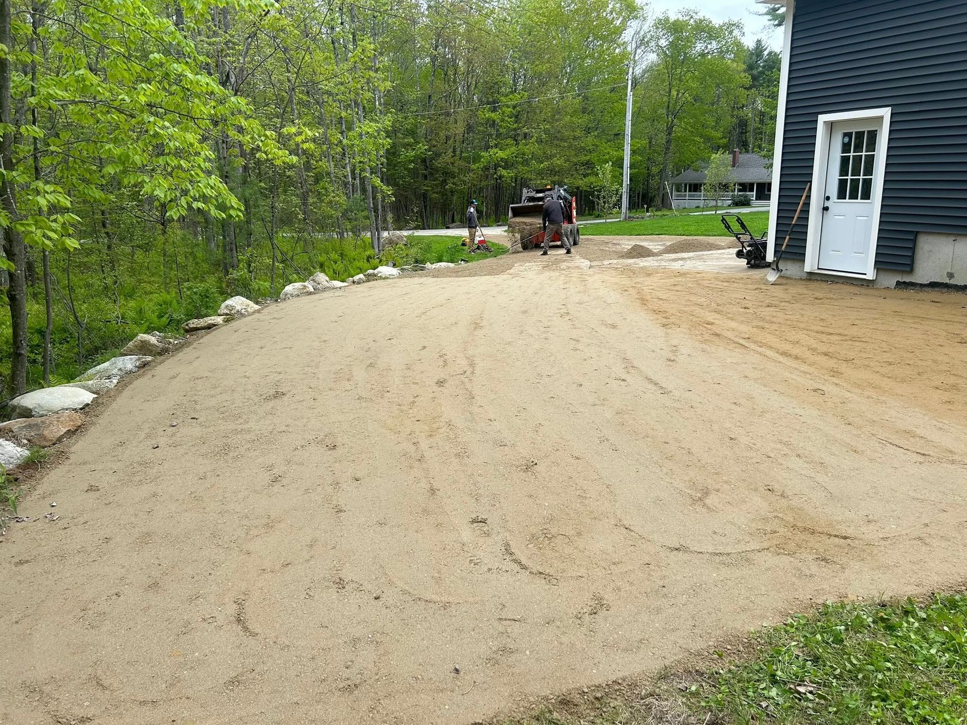 A dirt road leading to a house with trees in the background.