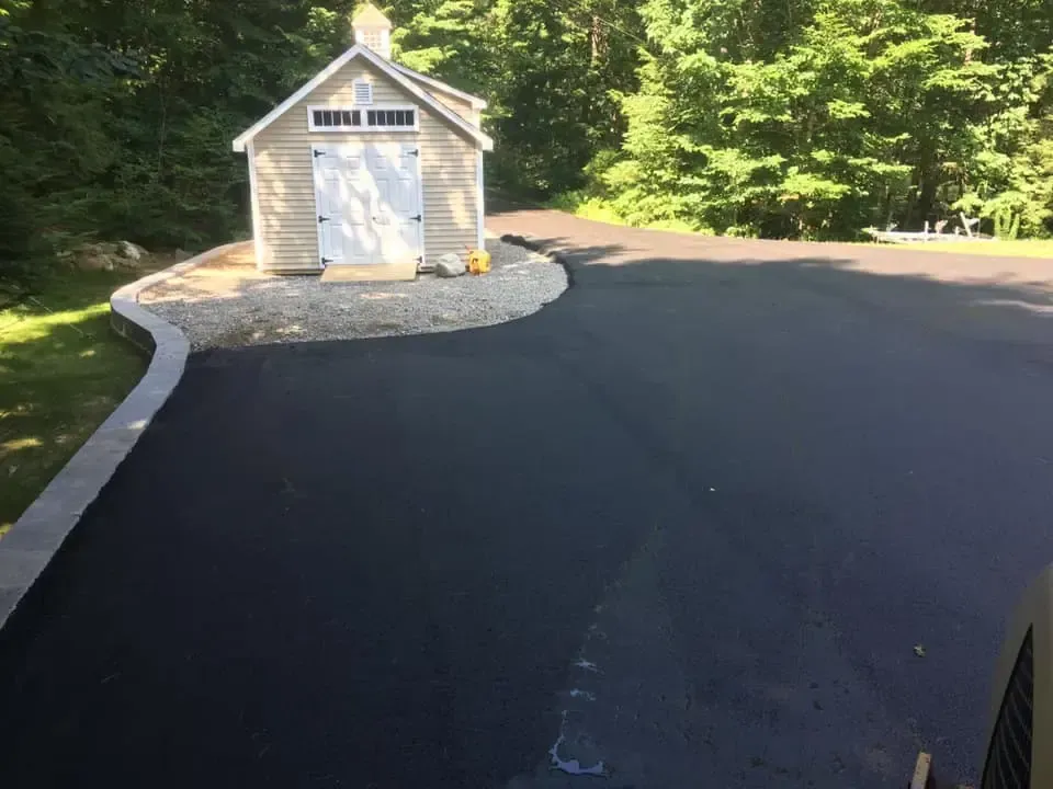A small shed is sitting on the side of a paved driveway.