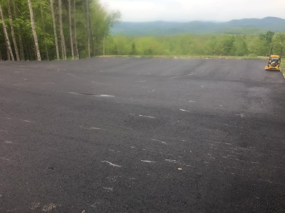 A large empty asphalt parking lot with trees in the background.