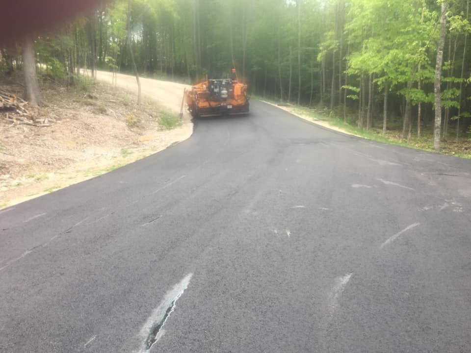 A tractor is driving down a road in the woods.