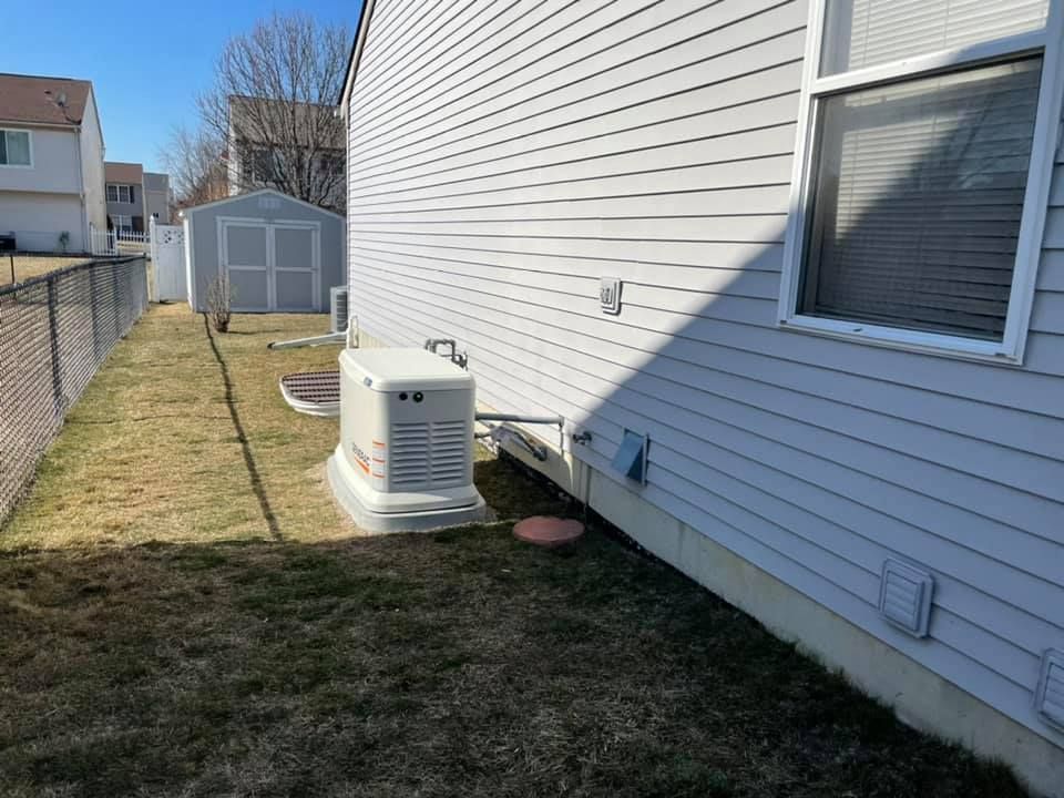 Side yard beside a white house, with an outdoor generator and a chain-link fence along the lawn.