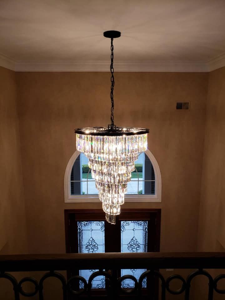 Crystal chandelier hanging in a beige foyer above a doorway and railing.