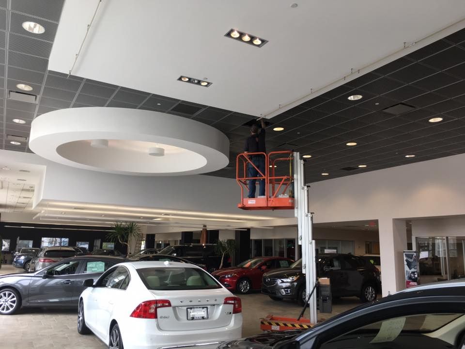 Car showroom interior with several parked cars and a worker on a red lift near the ceiling