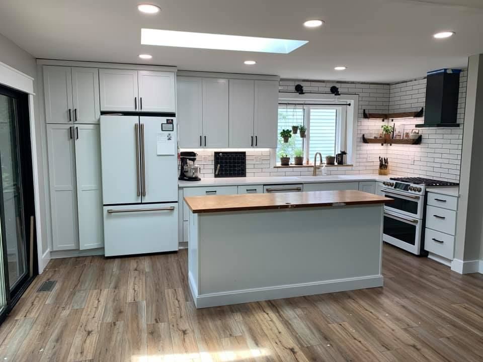 Bright modern kitchen with white cabinets, central island, stainless appliances, and wood flooring