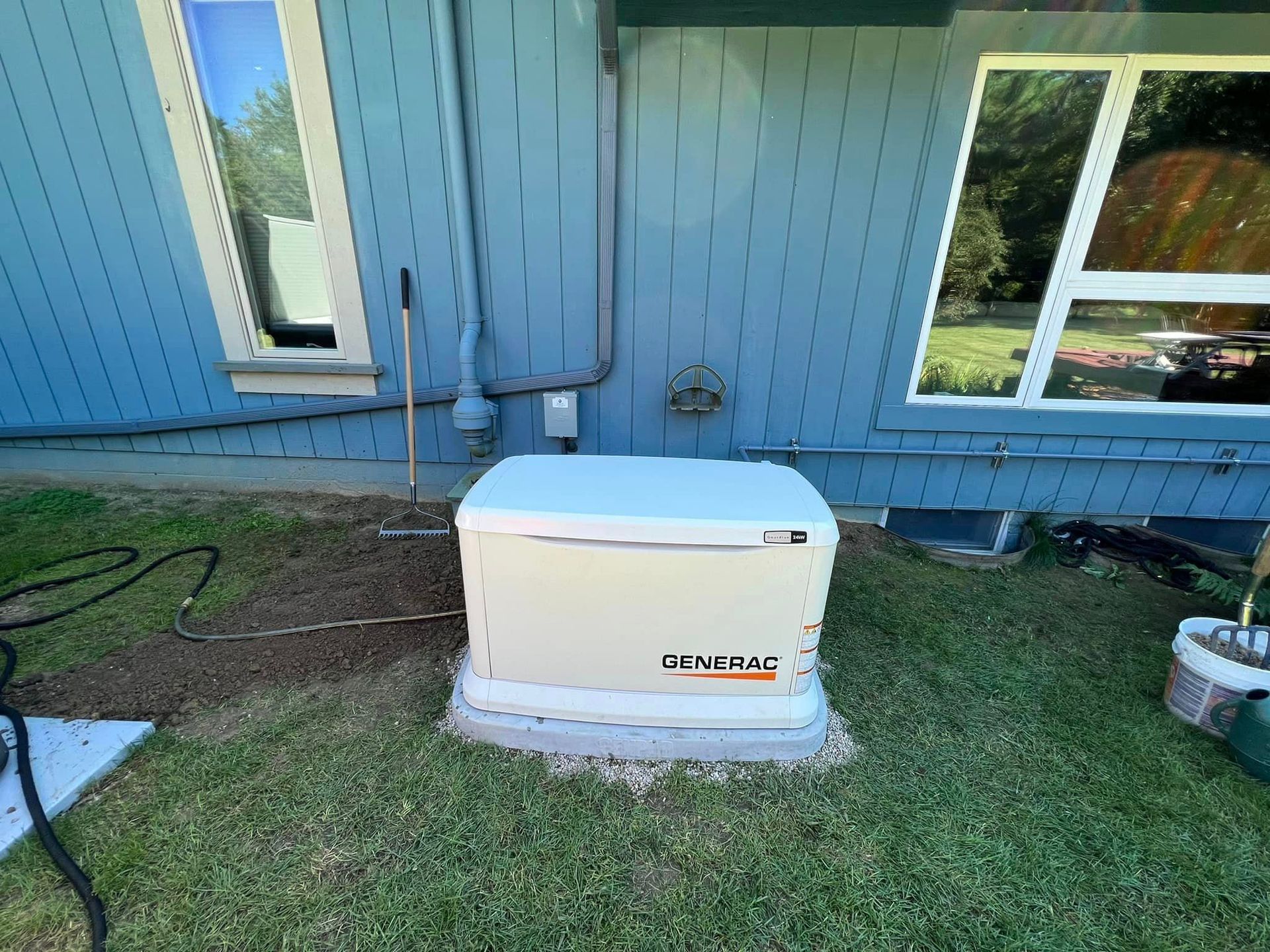 White Generac generator beside a blue house with windows and grass in the foreground