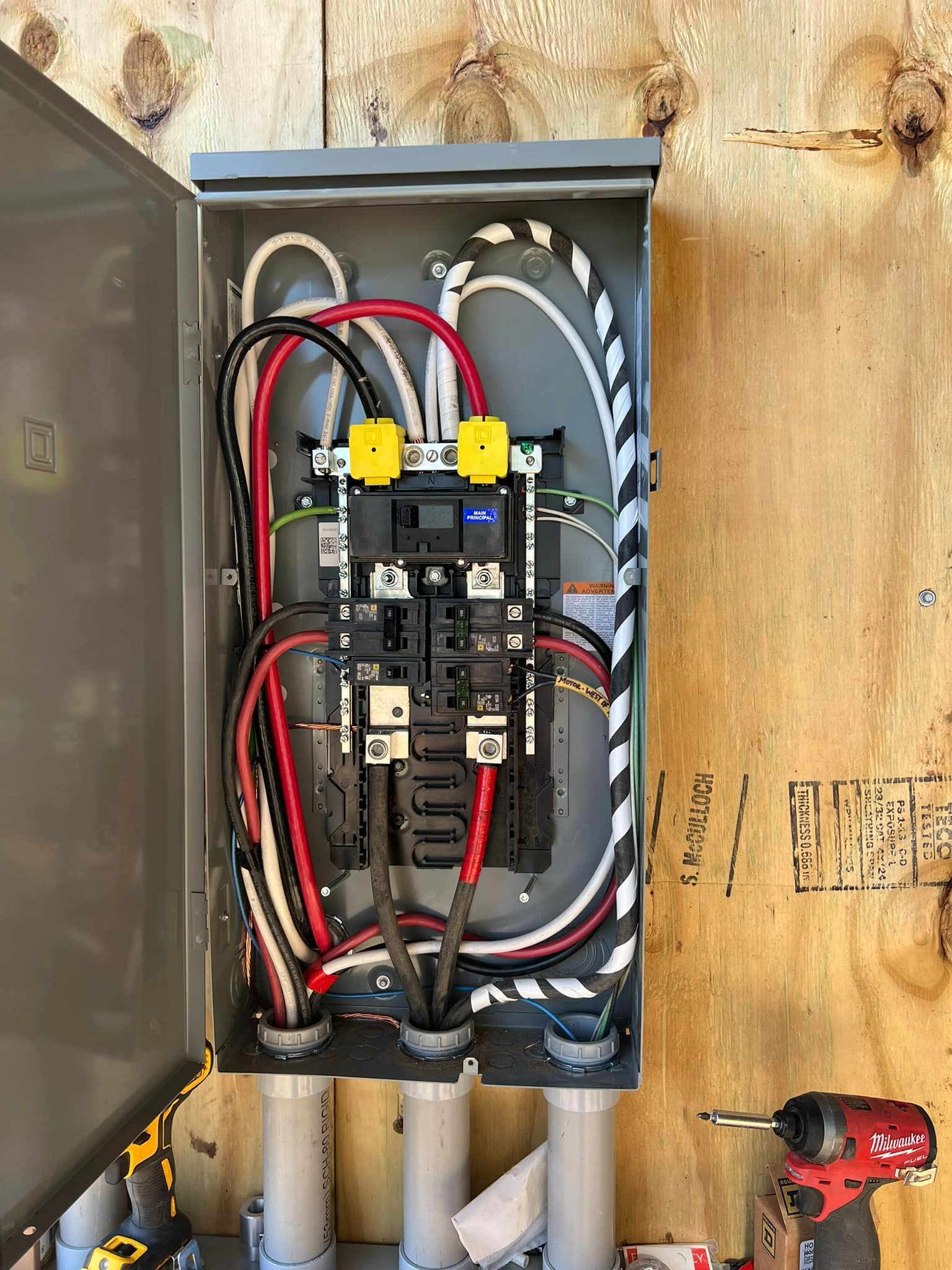 Open electrical breaker panel with red, black, and white wires mounted on a wooden wall.