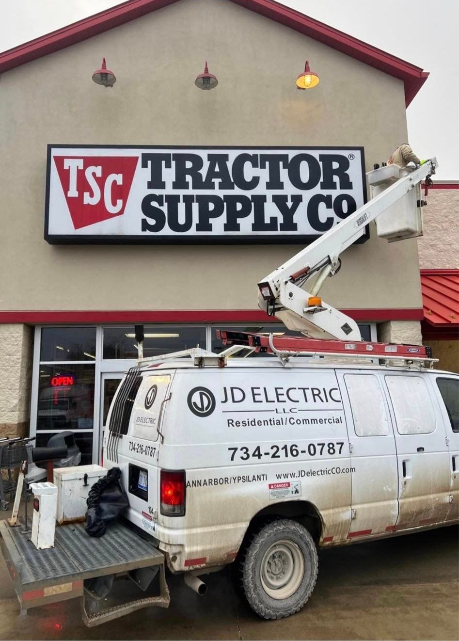 Utility truck at Tractor Supply storefront, using a lift to work near the sign.