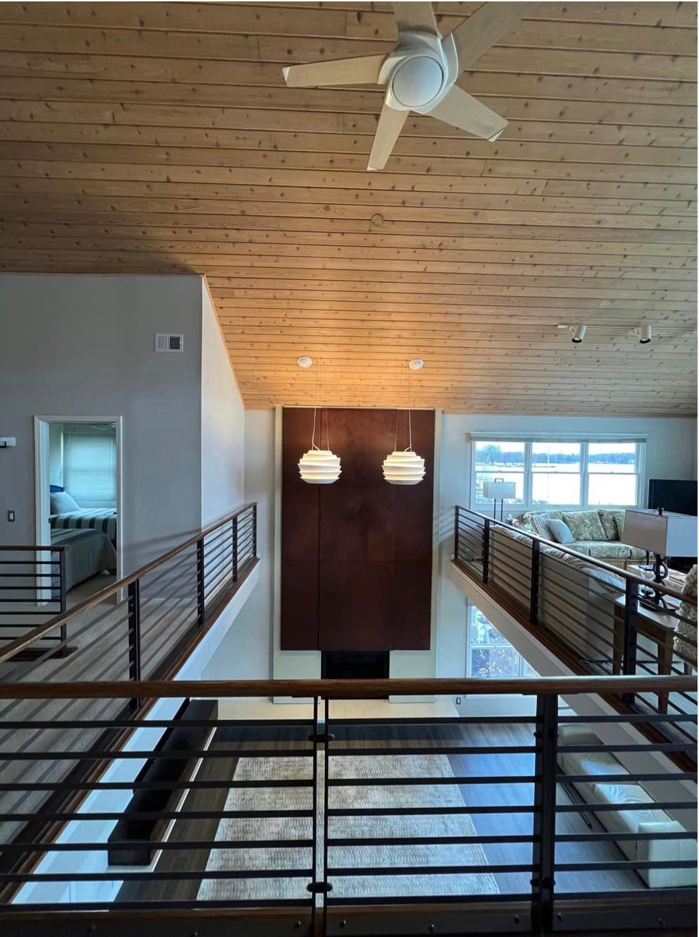 Modern interior hallway with railings, wood ceiling, pendant lights, and large windows at the far end