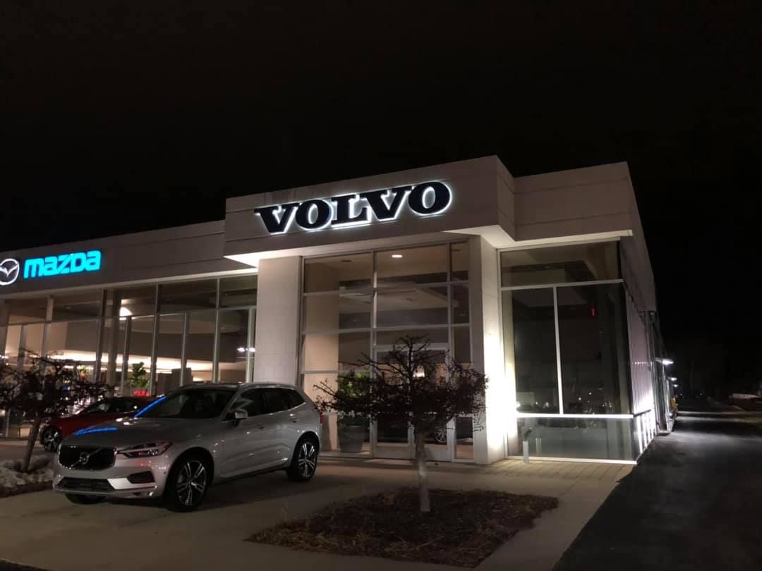 Volvo car dealership at night with illuminated showroom and a silver SUV parked outside