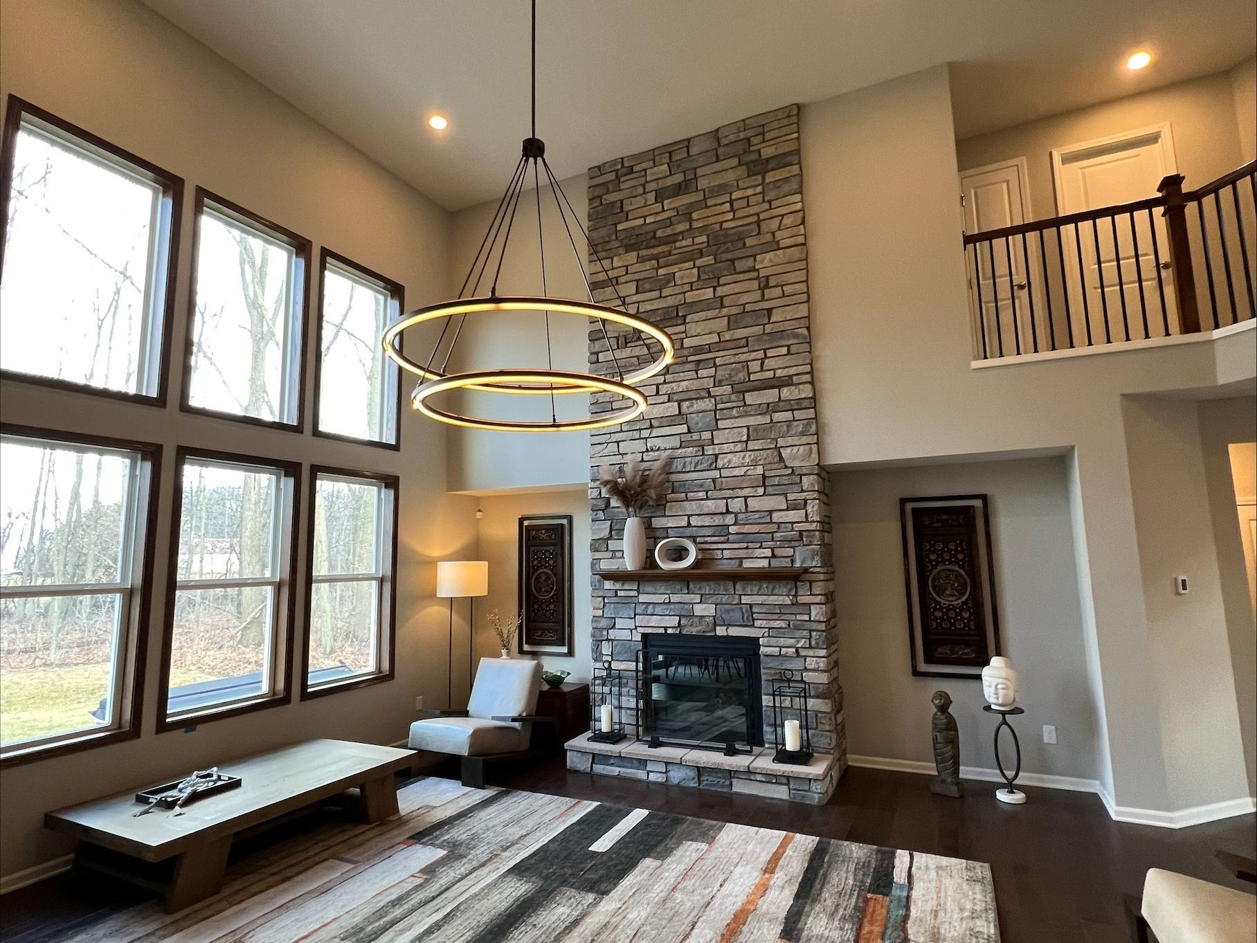 Bright living room with large windows, stone fireplace, and modern ring chandelier