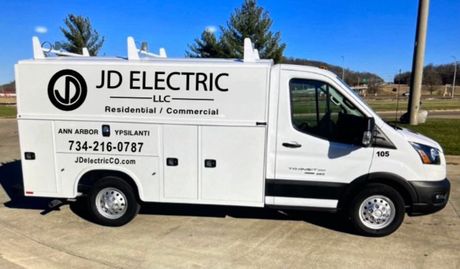White JD Electric service van parked outdoors on a sunny day, with company logo and phone number on the side