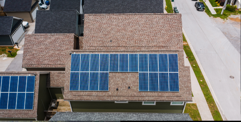 Aerial view of a house roof with multiple blue solar panels beside a residential street.