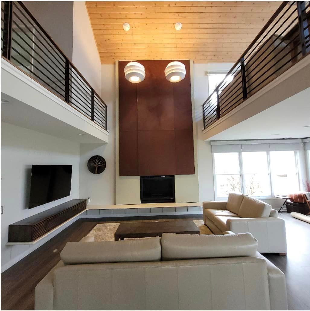 Modern living room with high wood ceiling, loft railings, fireplace, and beige sectional sofa.
