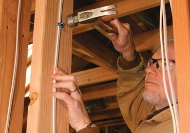 Person using a hammer to inspect wooden framing inside a construction site
