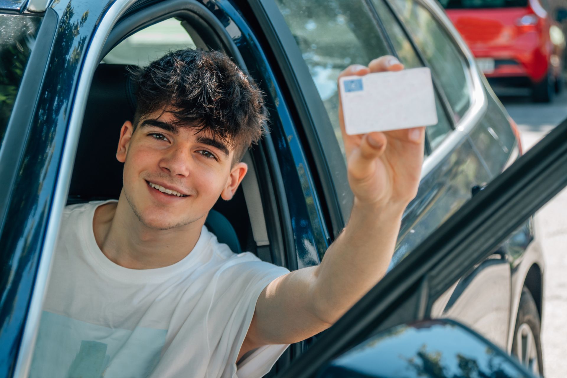 Smiling teen driver sitting in a car holding up his new driver's license