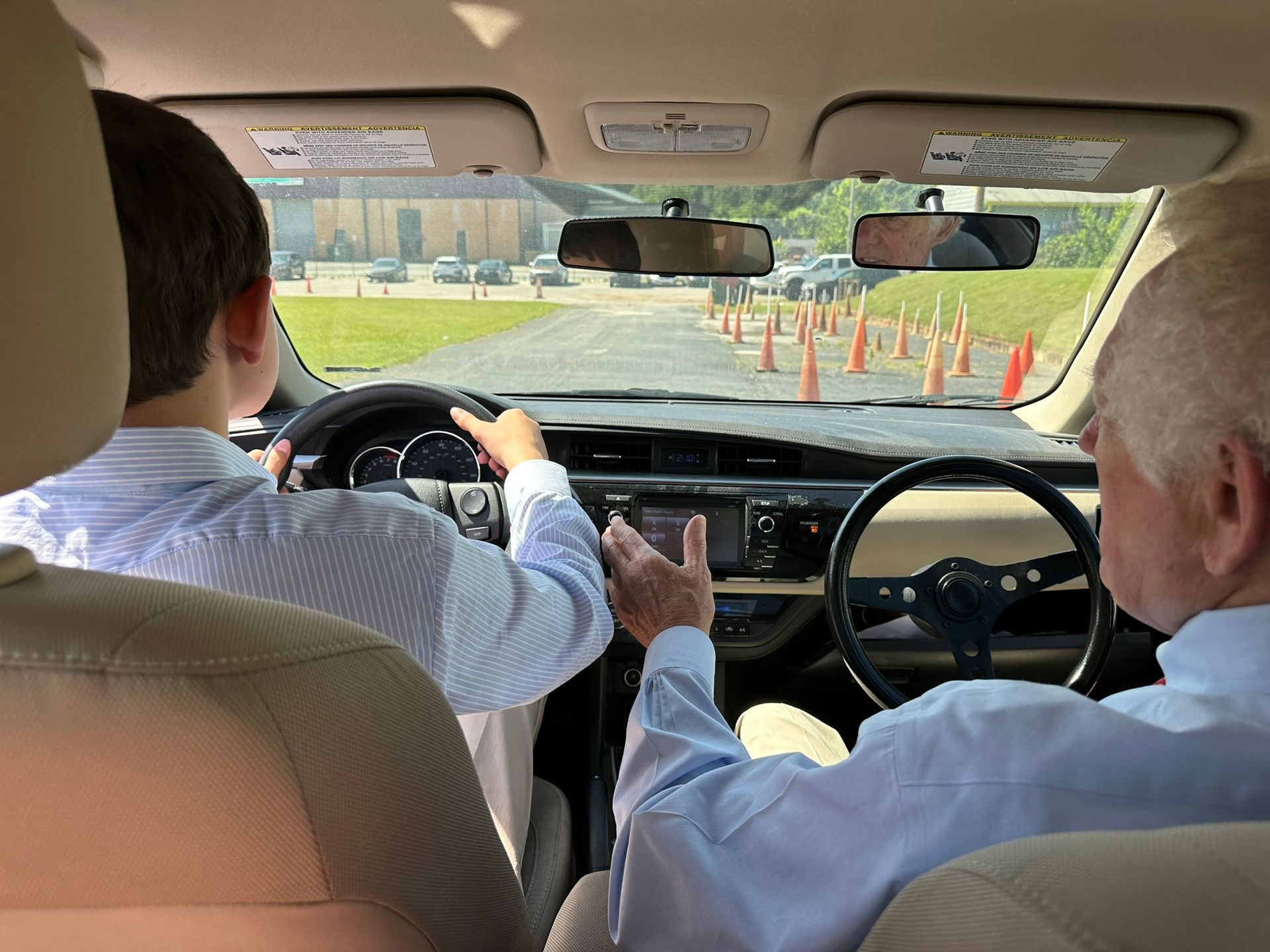 Two people in a car driving through a cone-lined course, viewed from the back seat.