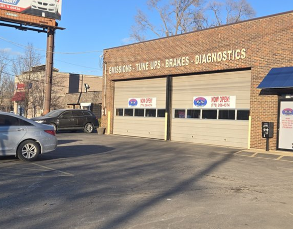 Auto repair shop exterior with garage bays, parked car, and signs for exhaust, tune-ups, brakes, and diagnostics | AACCEL Emissions & Auto Repair Specialists