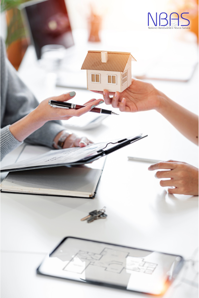A person is holding a model house in their hand while another person looks at a tablet.