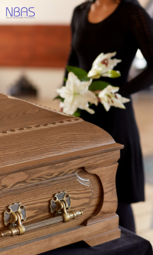 A woman is standing next to a wooden coffin holding flowers.