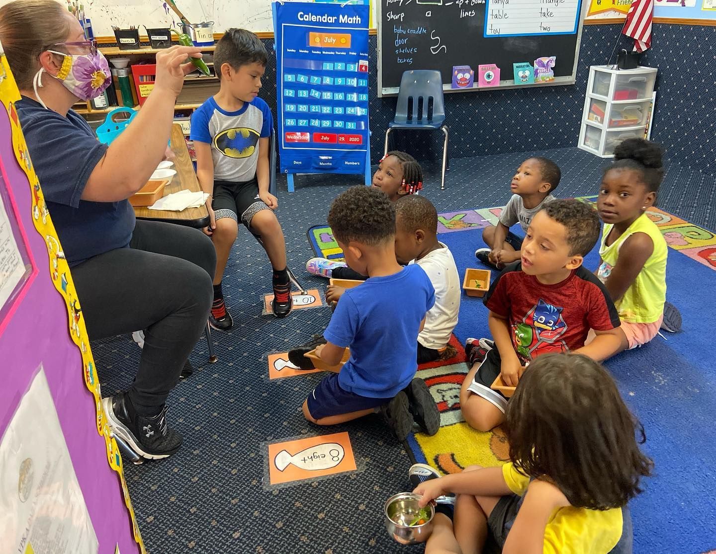 A group of children are sitting on the floor in a classroom with a teacher.