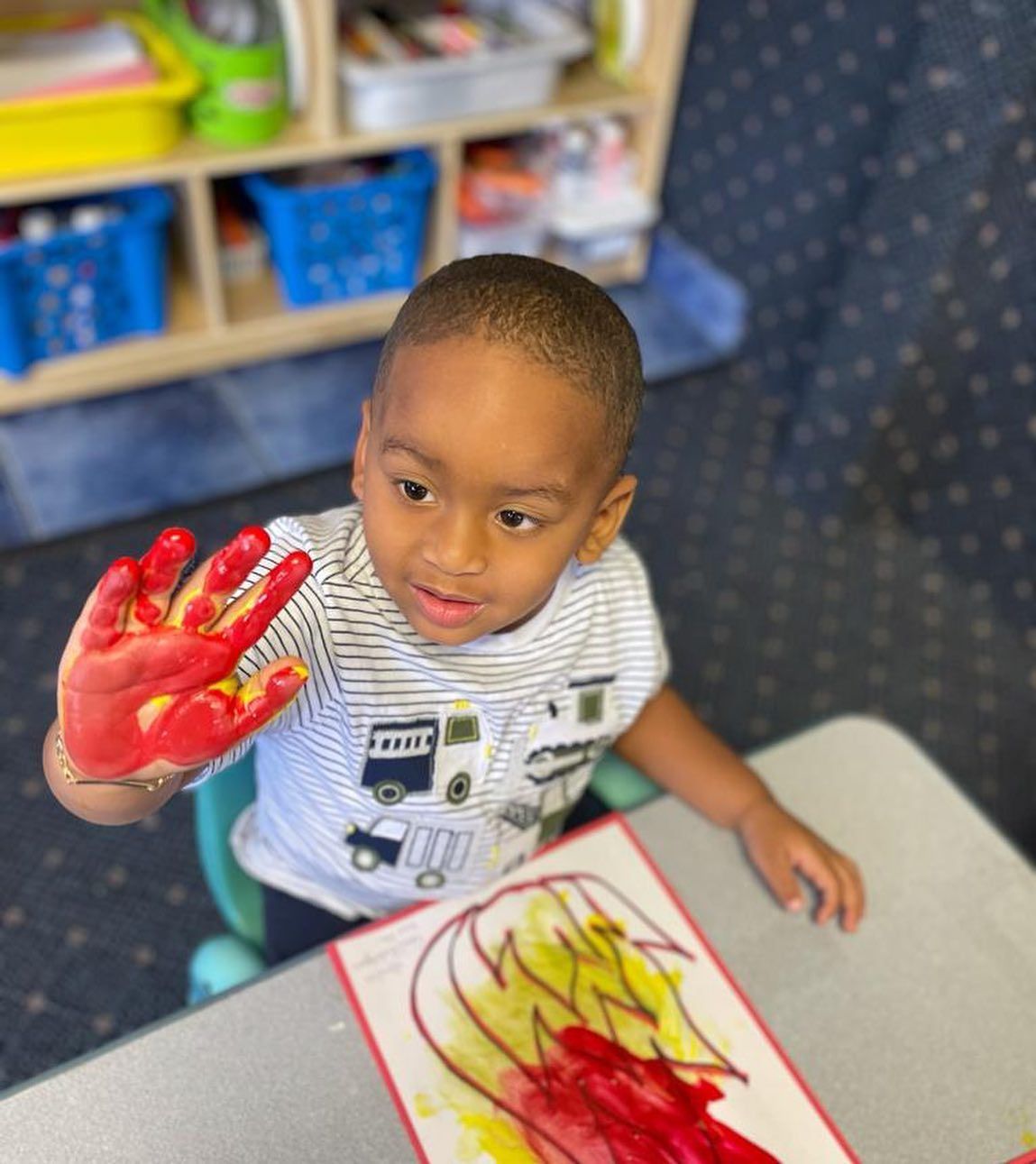 A young boy is sitting at a table with his hands painted red.