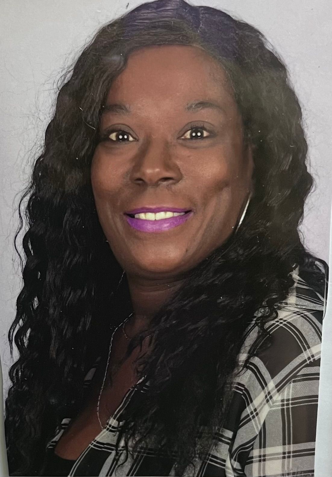 A woman with long black hair and purple lipstick is smiling for the camera.