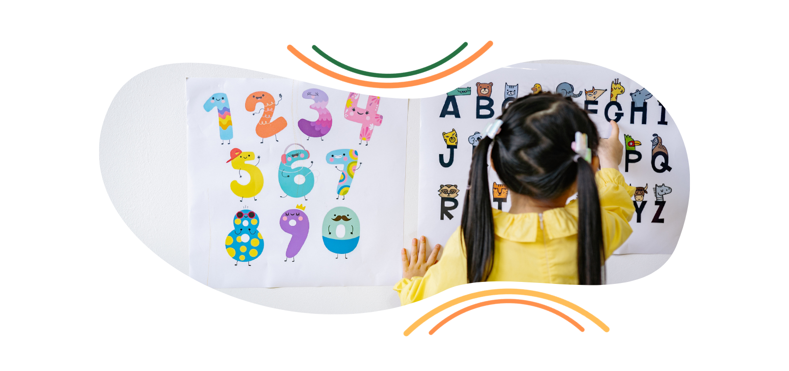 A little girl is standing in front of a wall with numbers and letters on it.