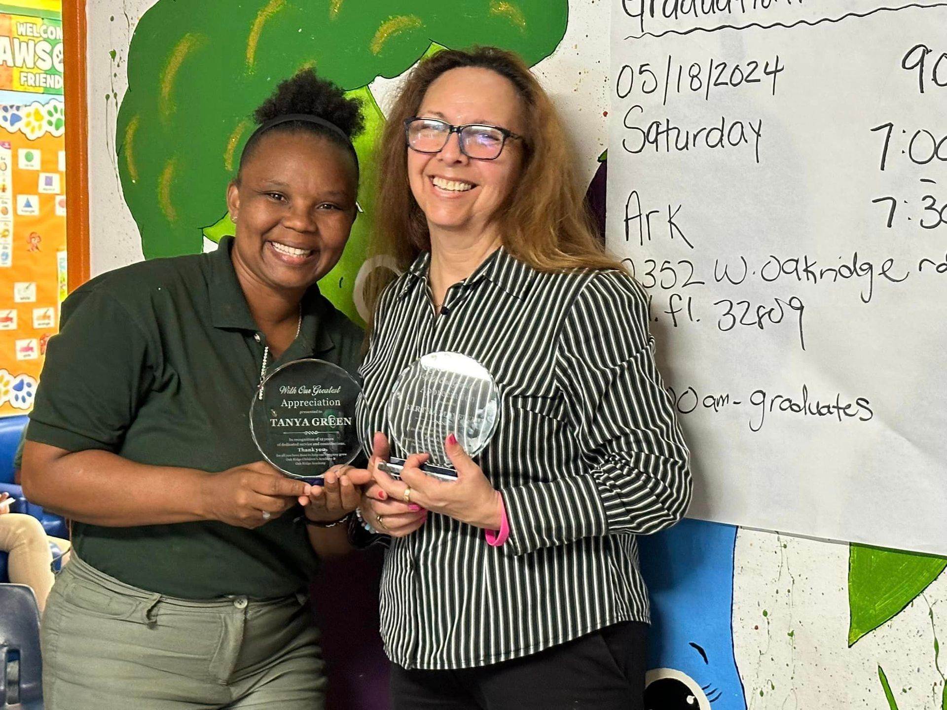 Two women are standing next to each other holding trophies.