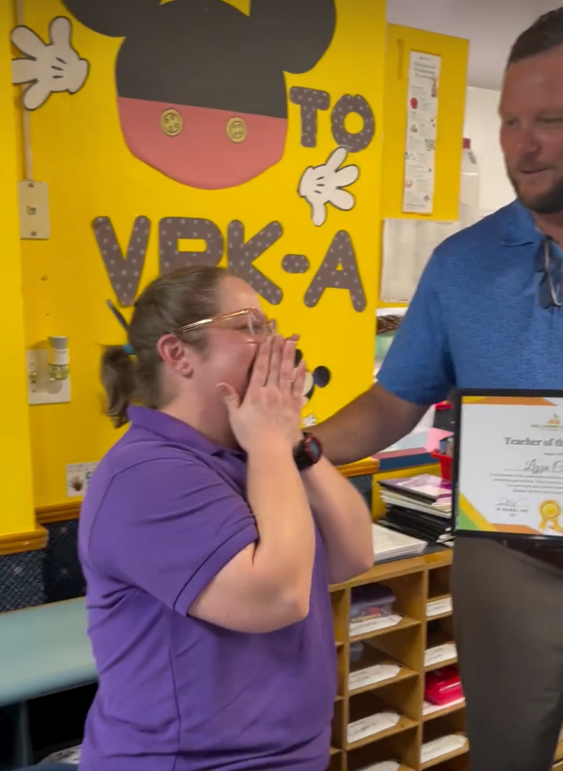 A man is giving a woman a certificate in front of a yellow wall that says vpk-a