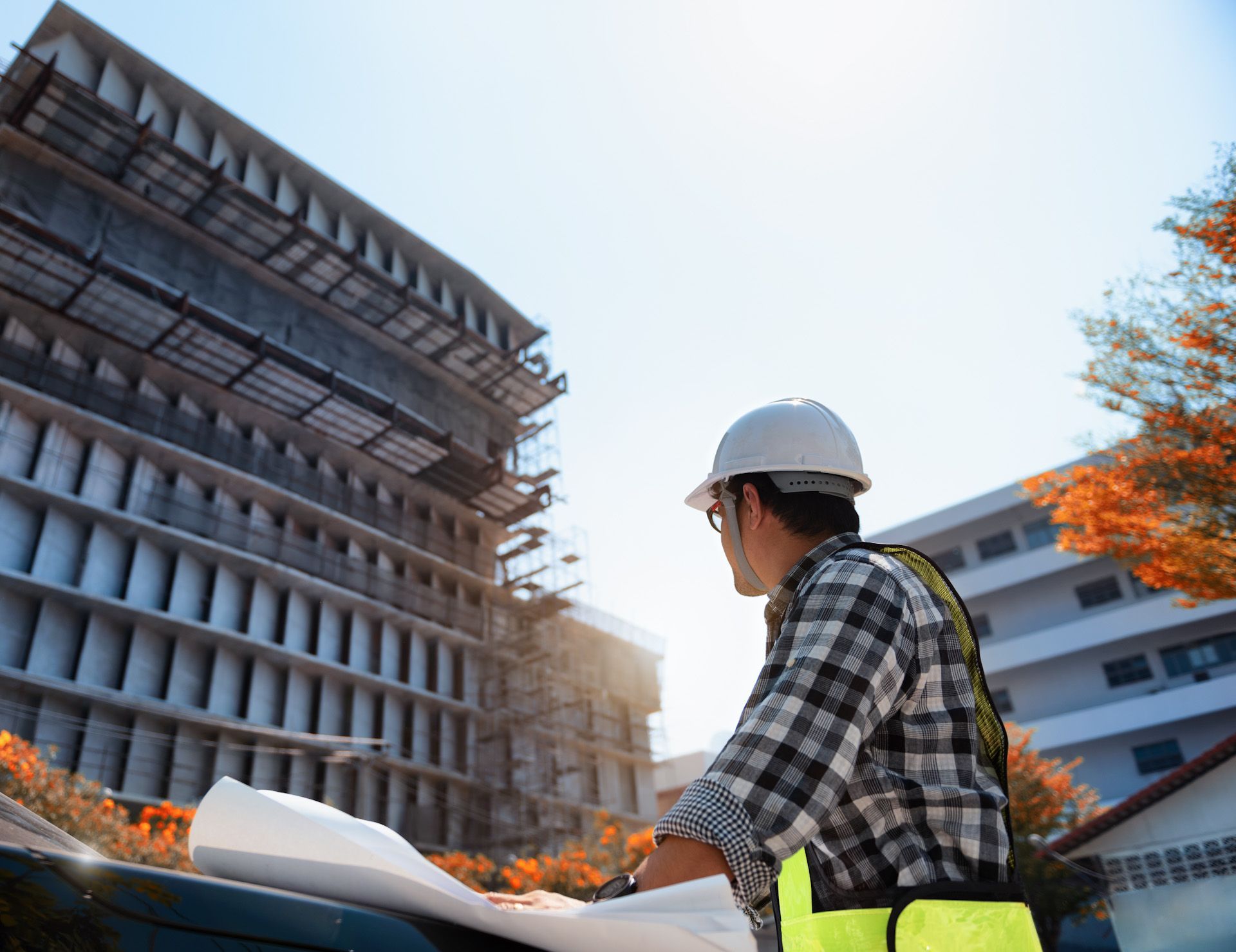 A construction worker is looking at a blueprint in front of a building under construction.