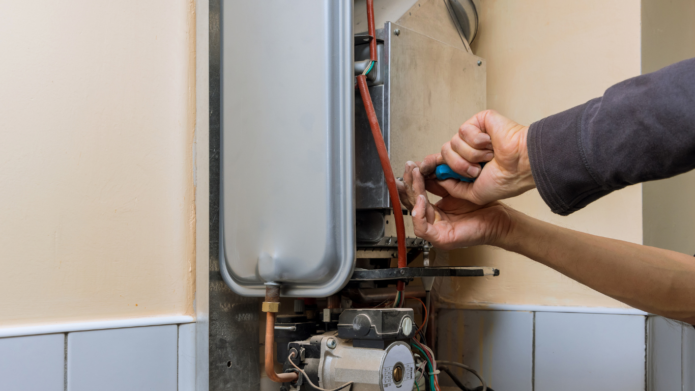 Person using a screwdriver to repair a furnace; indoor setting with beige walls.