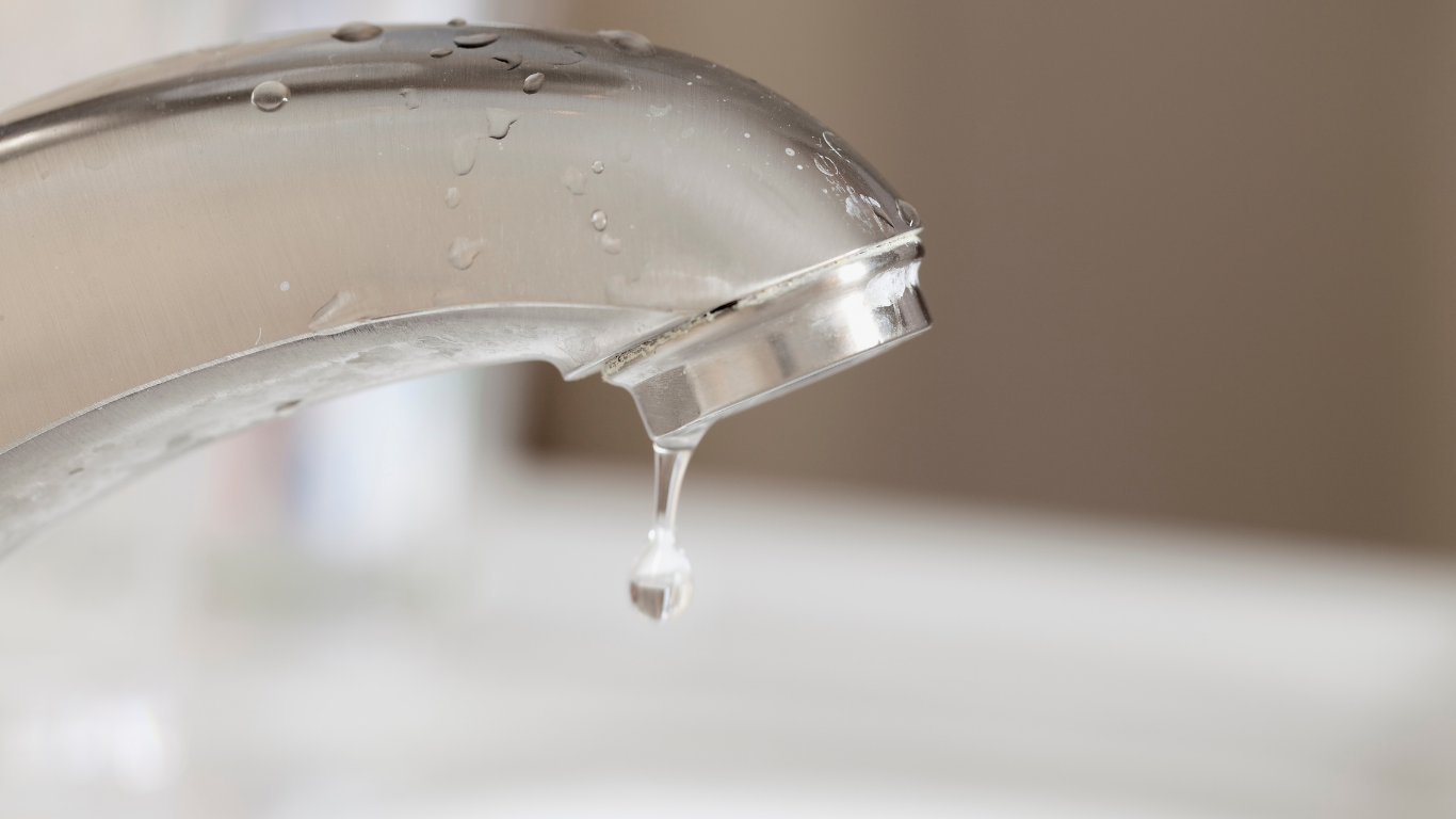 Faucet with water droplet falling. Shiny chrome faucet, blurred background.