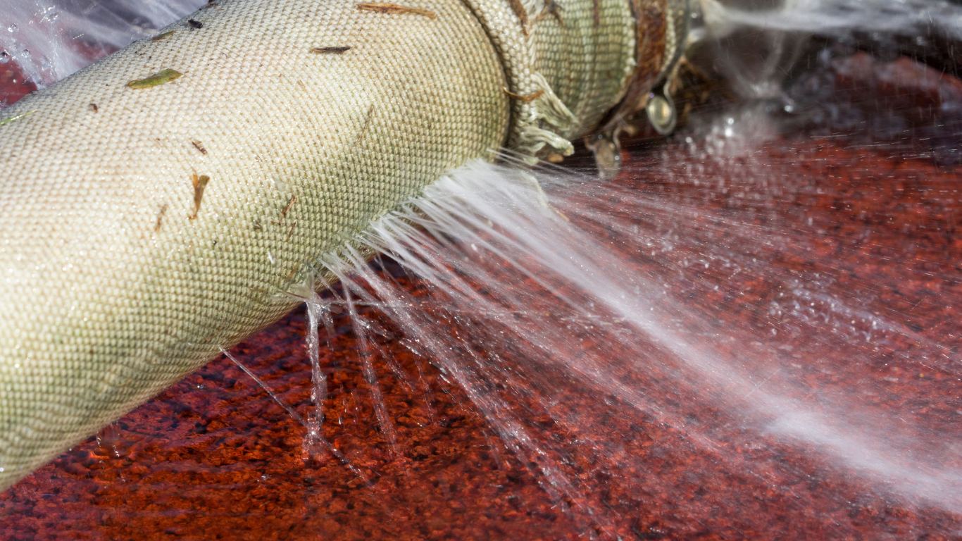 Leaking water hose sprays water on red ground.