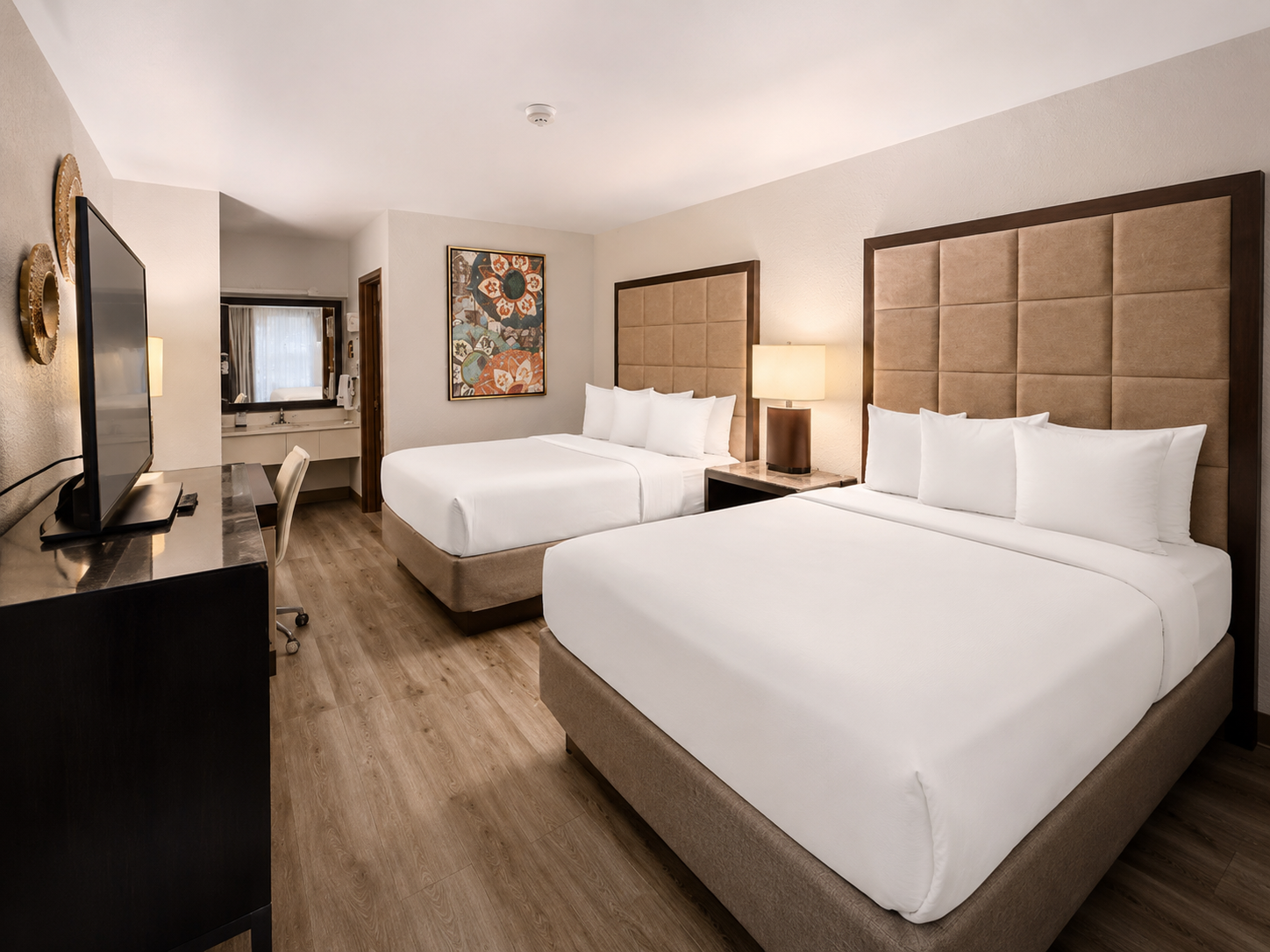 Hotel room with two queen beds, beige headboards, desk, and wall art