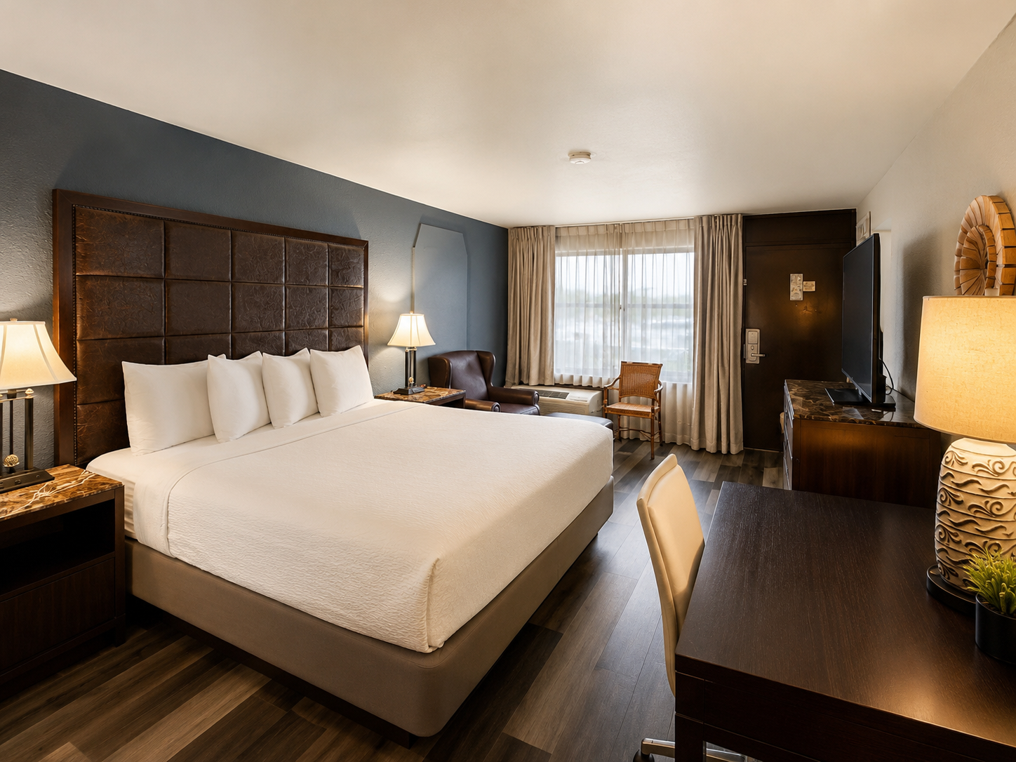 Spacious hotel room with a king bed, dark wood furniture, and a window with curtains.