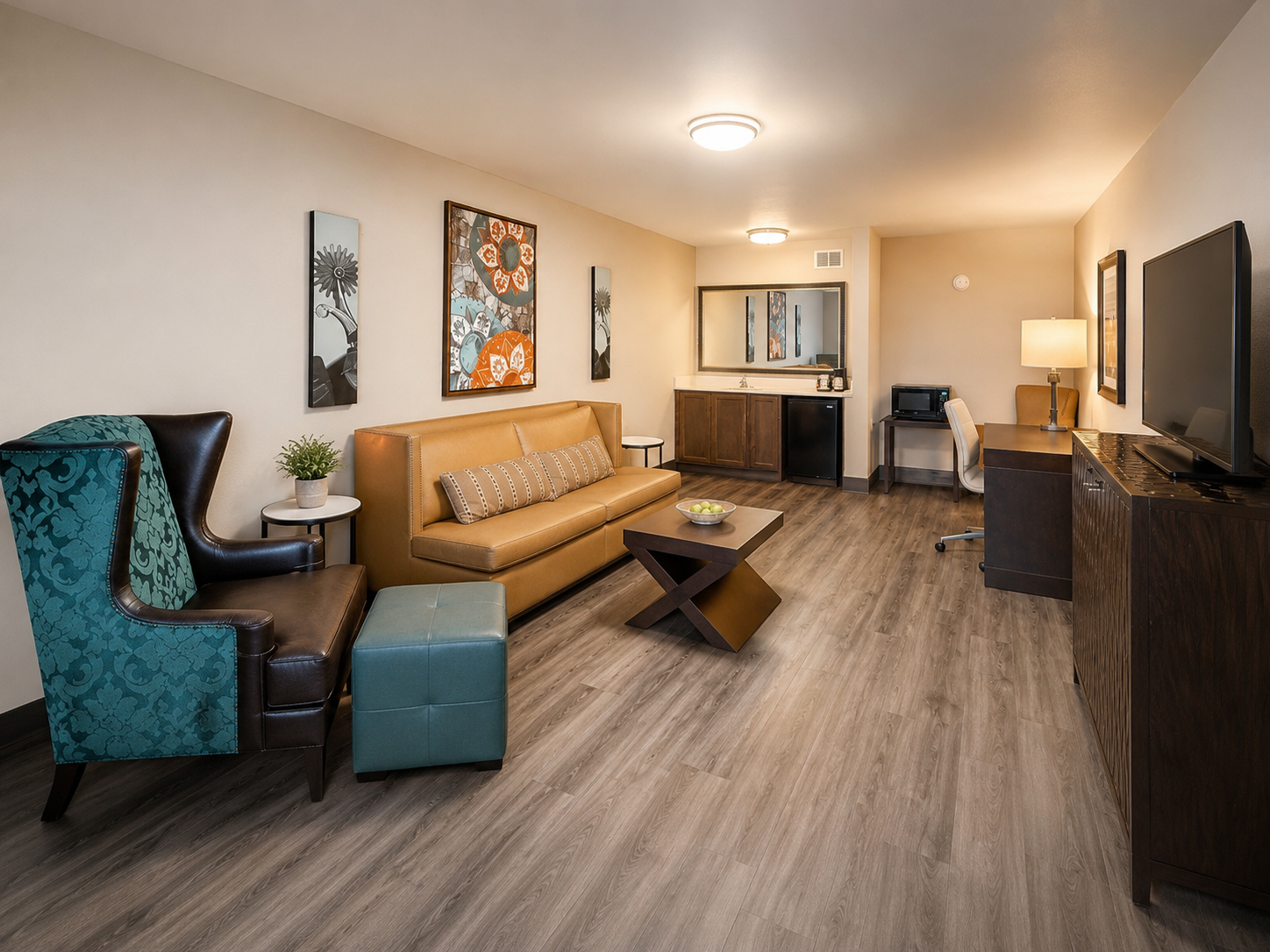 Modern living room with tan sofa, teal chair, wall art, TV, and open kitchen area