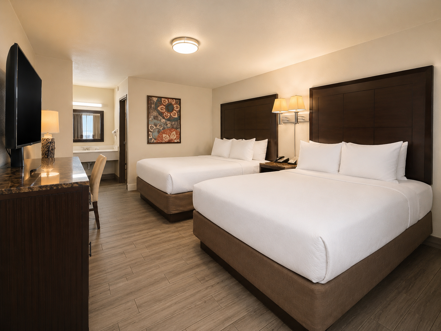 Hotel room with two queen beds, TV, desk, and warm lighting