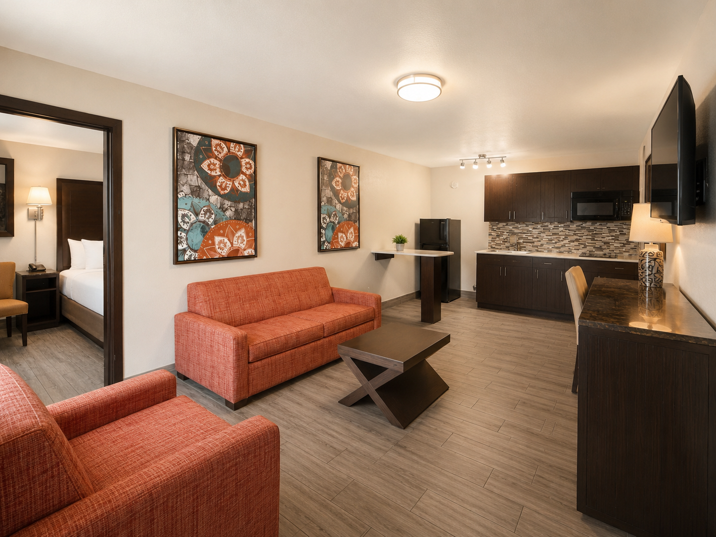 Modern studio room with orange sofas, desk nook, kitchenette, and wall art