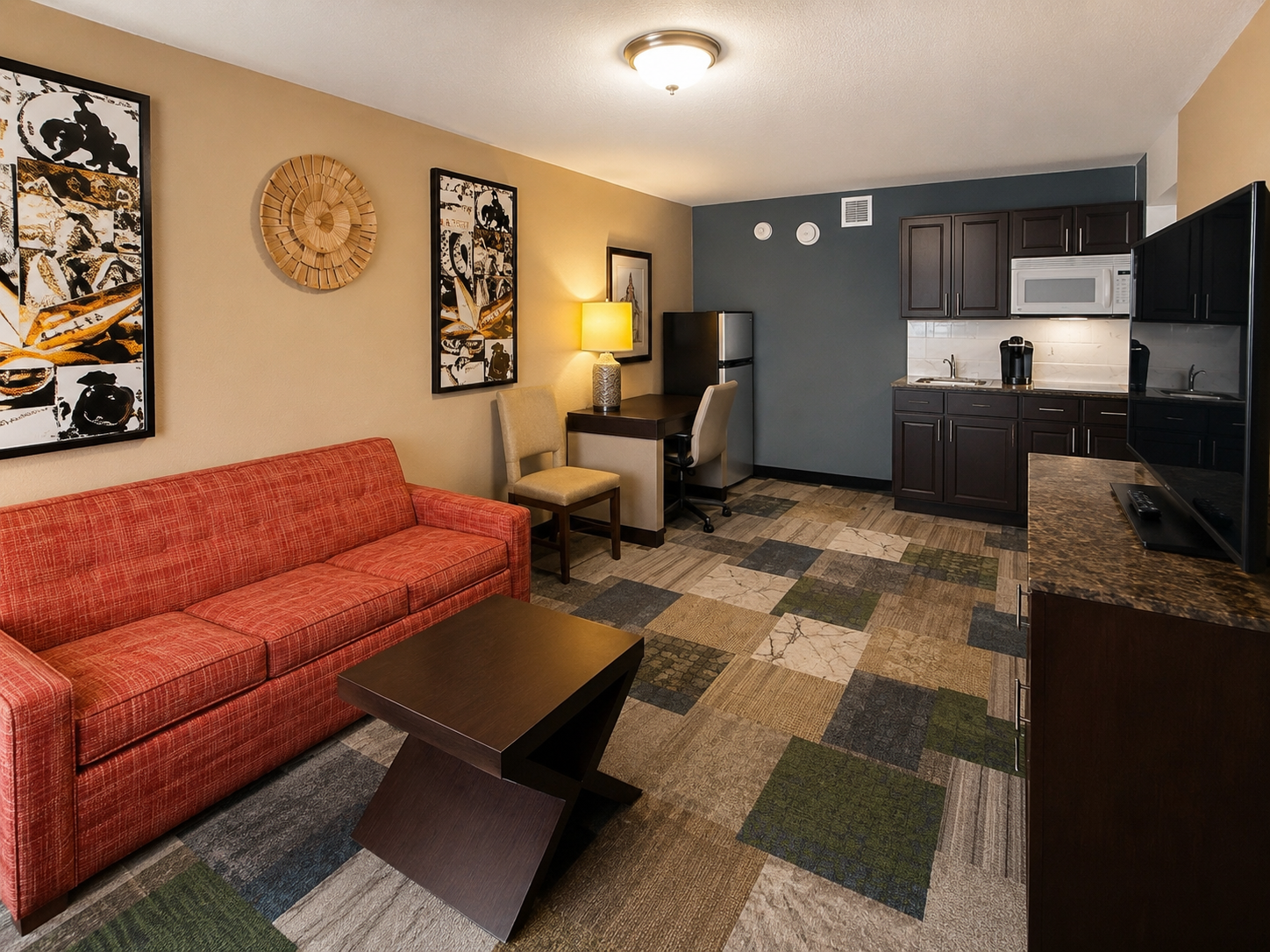 Small living room with red sofa, dark coffee table, rug, and compact kitchen area.