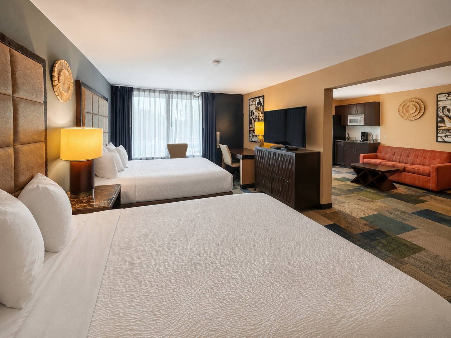 Hotel room with two beds, TV, dresser, lamp, and a sitting area by the window