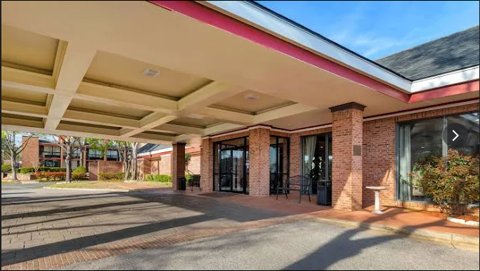 Covered brick building entrance with canopy and glass doors, sunny exterior driveway area