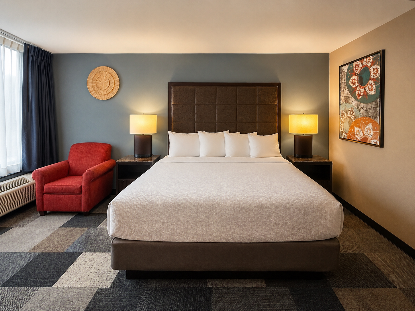Hotel room with king bed, red chair, lamps, and geometric carpet