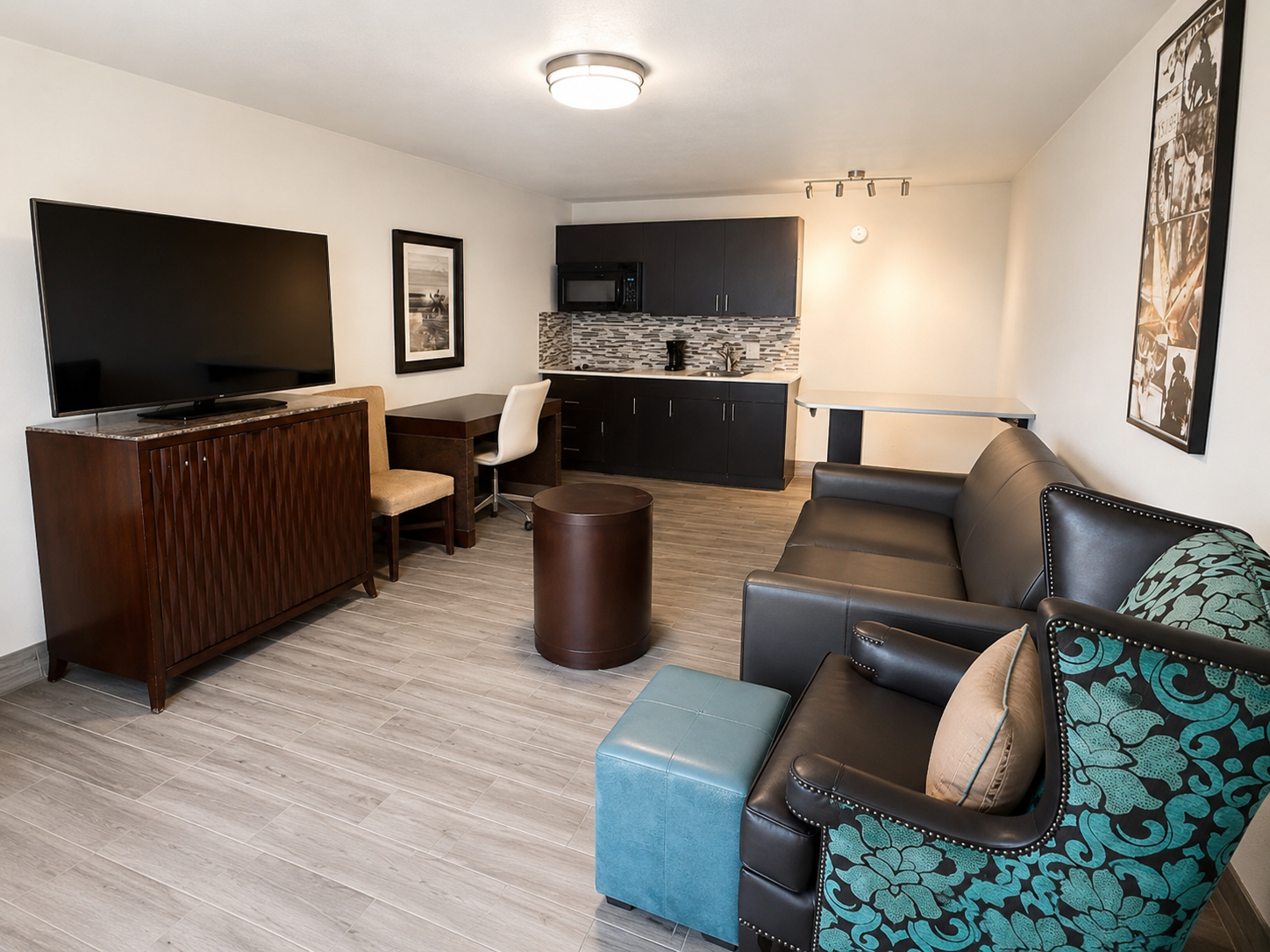 Modern living room with gray sectional, blue ottoman, TV, and small kitchenette area