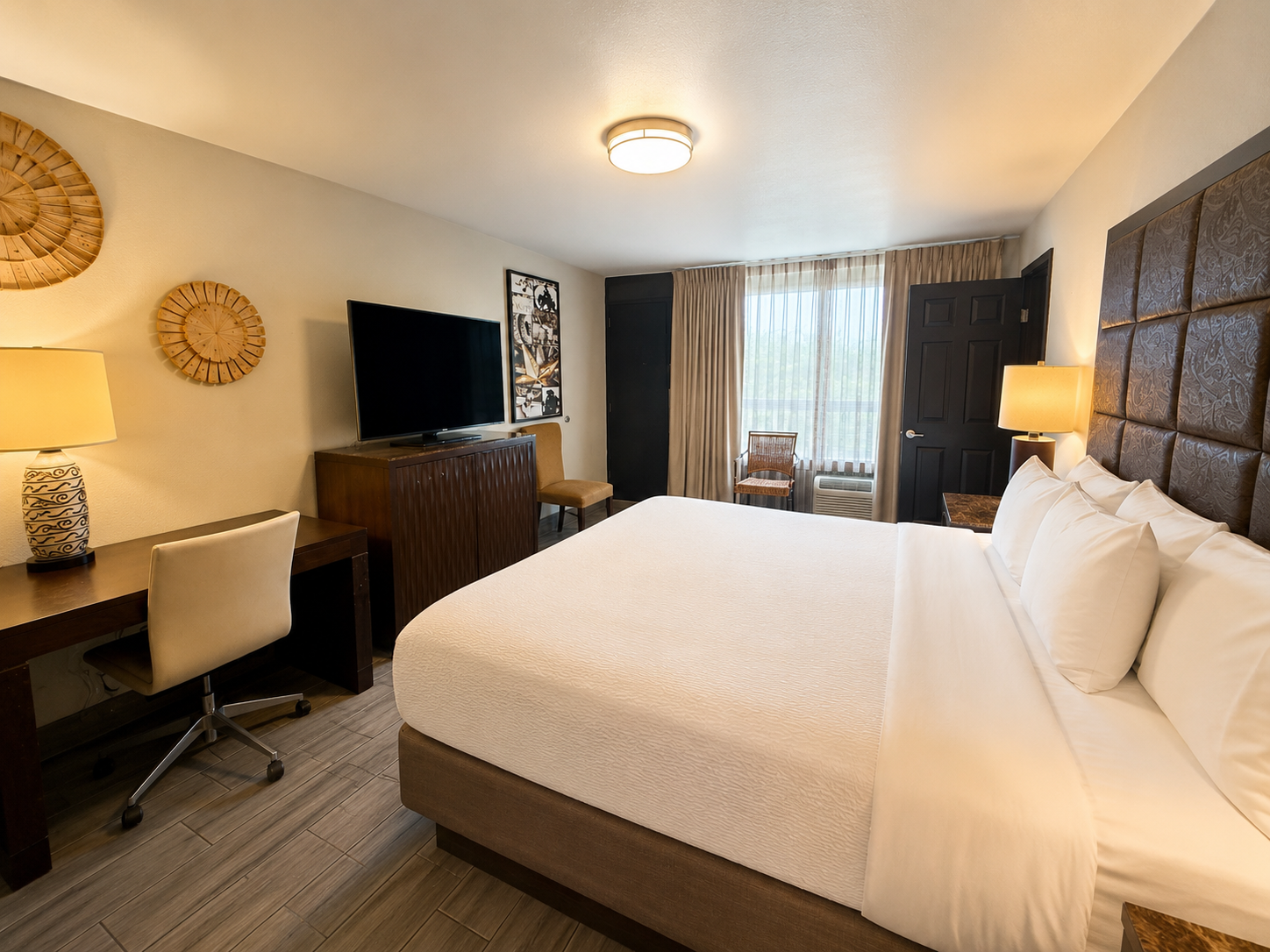 Hotel room with king bed, desk, TV, and window seating in neutral tones